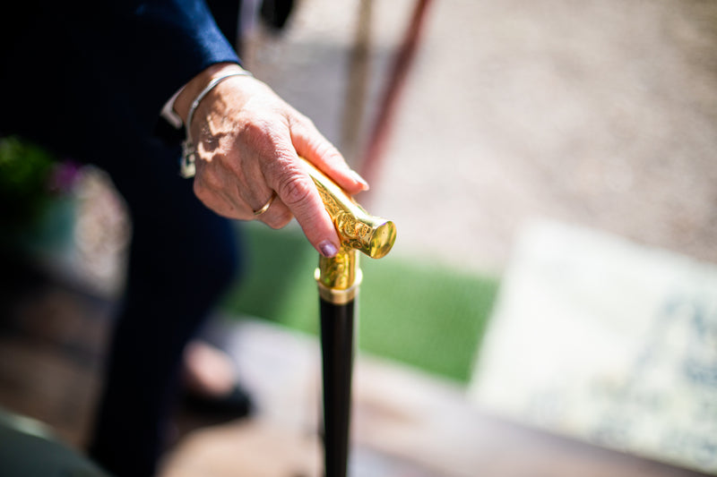 Close-up of a hand holding a gold-handled walking cane with a blurred background