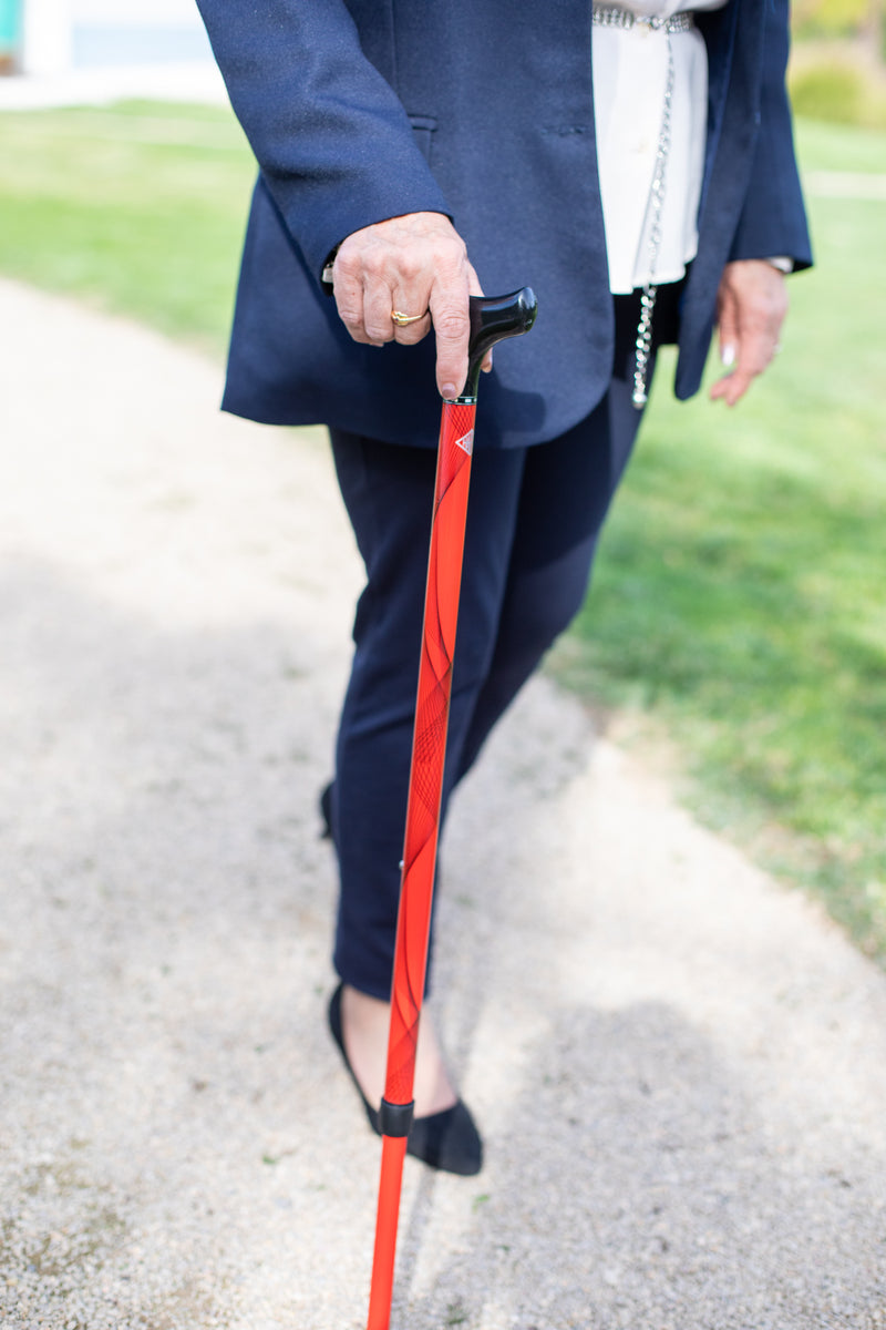 Person holding a red cane on a path with grass in the background